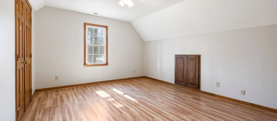 Empty apartment room with a hardwood floor, closet doors and a ceiling fan