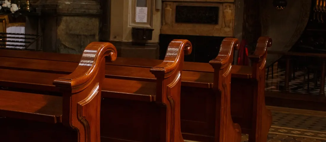 Rows of polished wooden pews inside a church with a tiled aisle floor