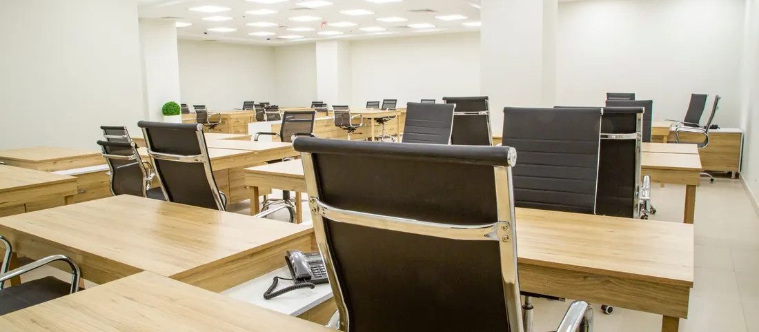 Rows of wooden desks and black office chairs in a bright office