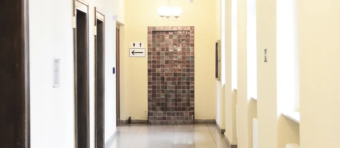 Bright building corridor with wooden doors, tall windows and a tiled floor