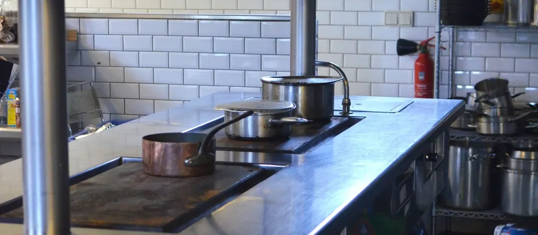 Empty commercial kitchen with stainless counters and white tiled walls