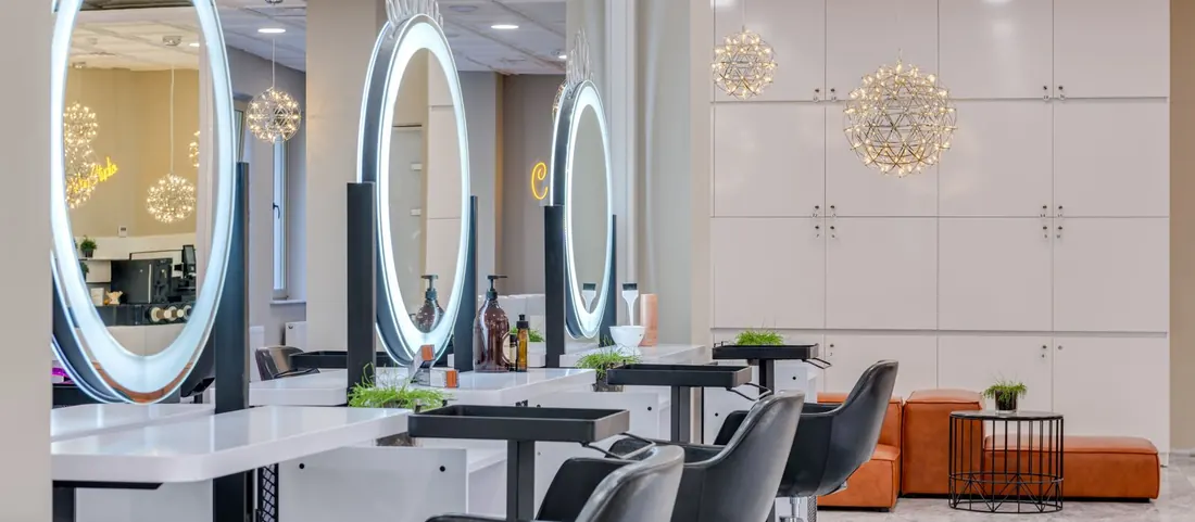 Salon styling stations with lit oval mirrors and black swivel chairs