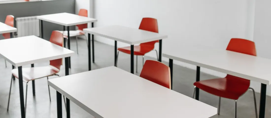 Classroom with white tables, red chairs and a pinboard on the wall