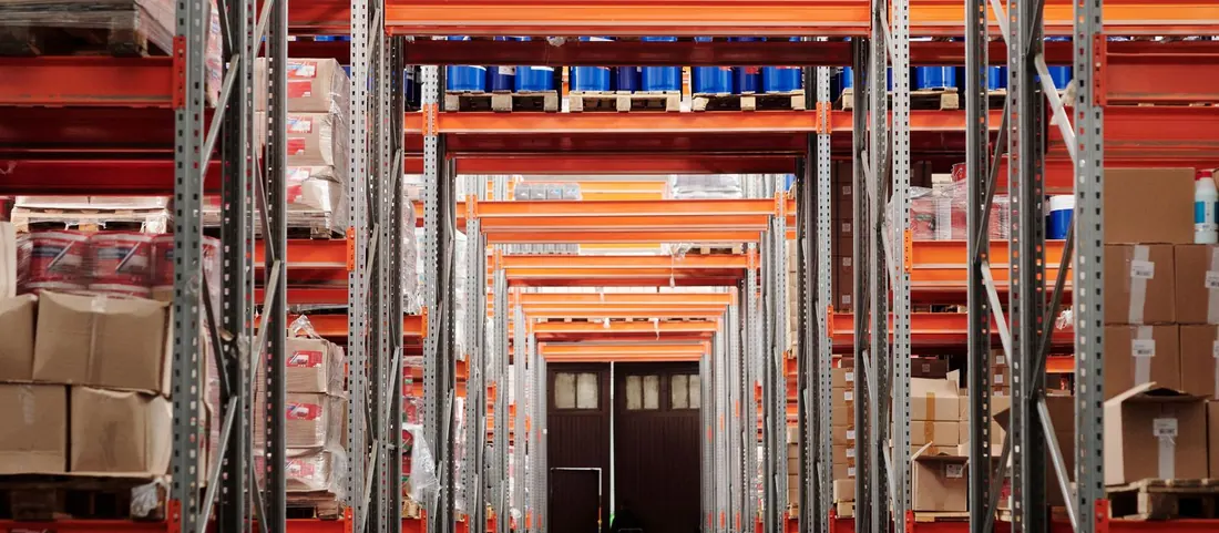Warehouse aisle between tall orange pallet racks stacked with goods