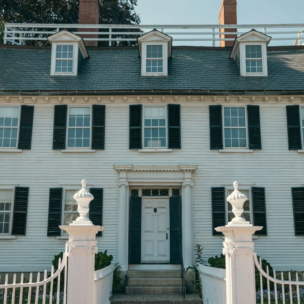 White clapboard colonial house with black shutters, dormers and a brick chimney
