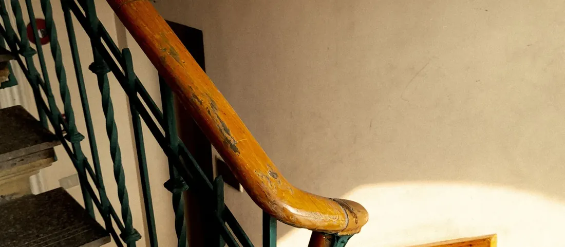 Apartment stairwell with a worn wooden handrail and green iron balusters