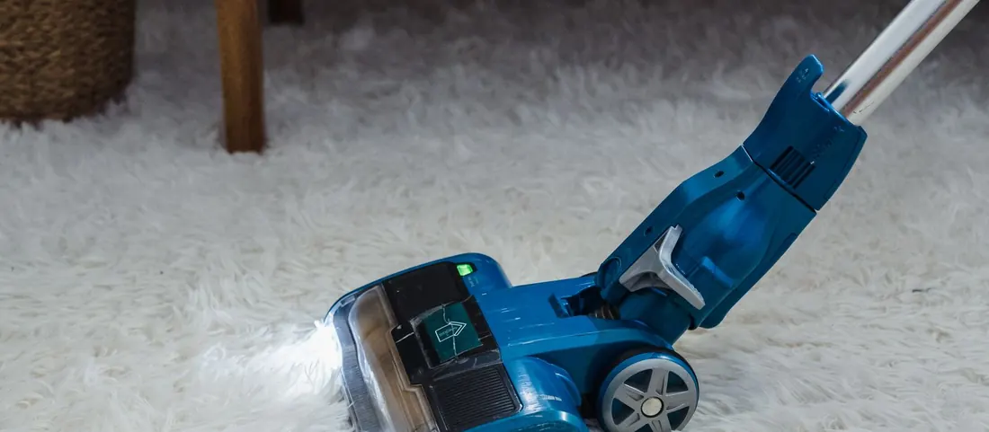 Blue upright cleaning machine with its light on part way across a thick cream carpet