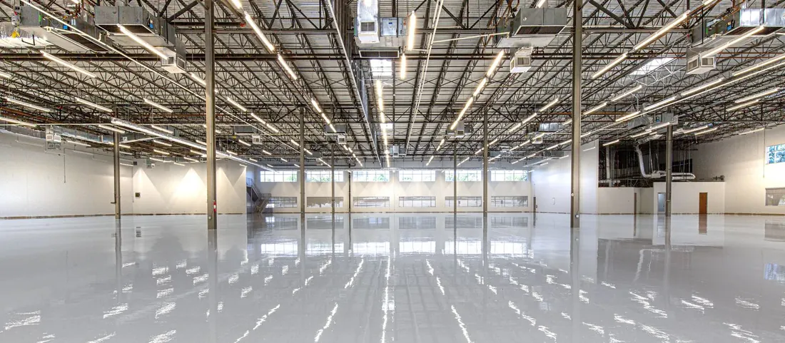 Glossy grey resin floor reflecting the ceiling lights of a large empty warehouse