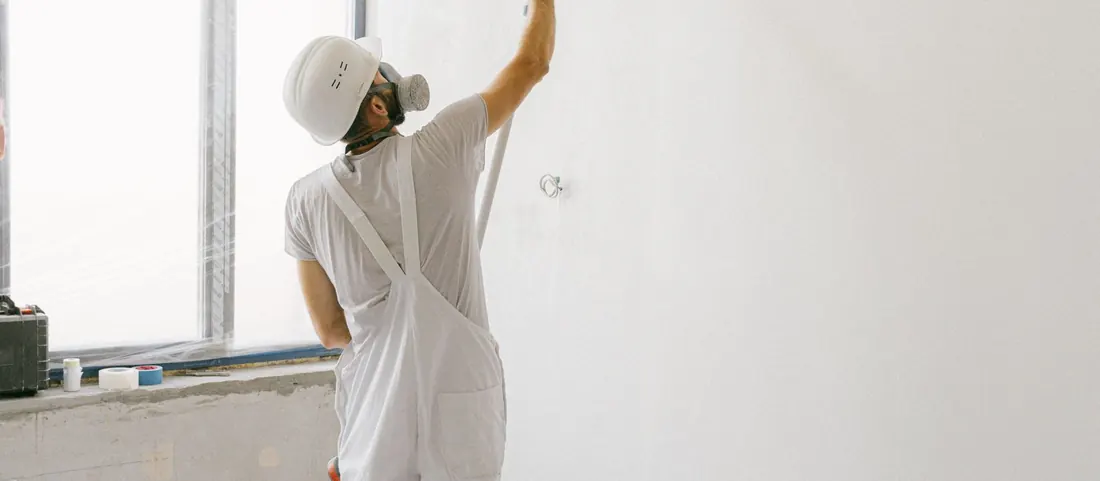 Painter in white overalls rolling a ceiling edge with an extension pole