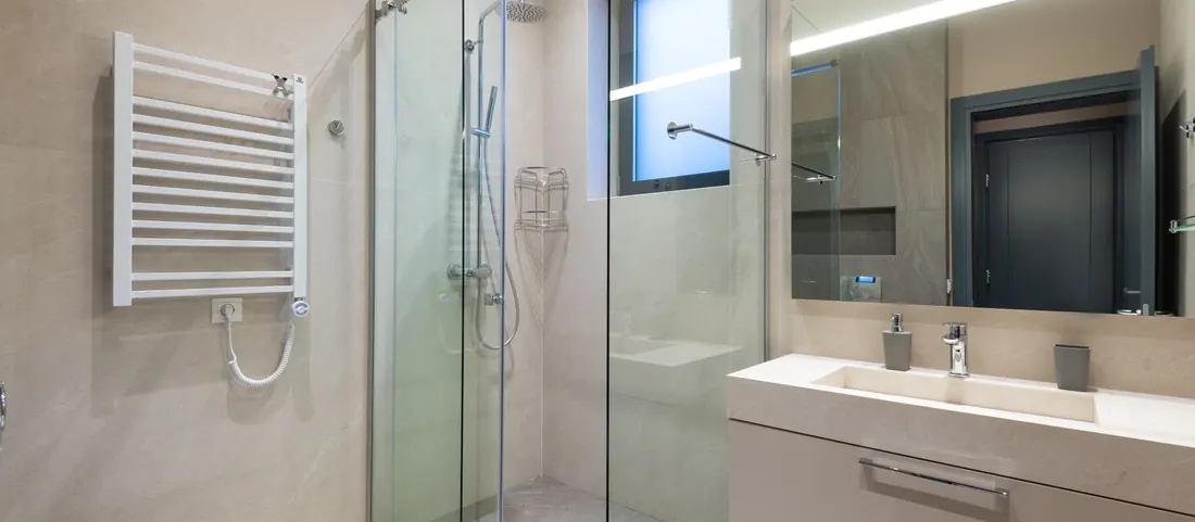 Clean tiled bathroom with a glass shower, vanity sink and wide mirror