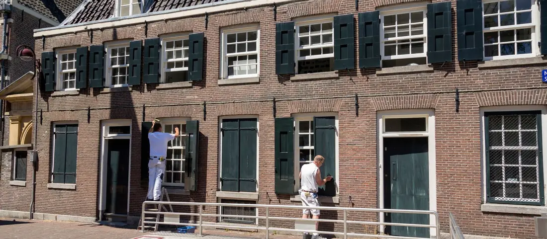 Two painters working on the windows and shutters of a brick house