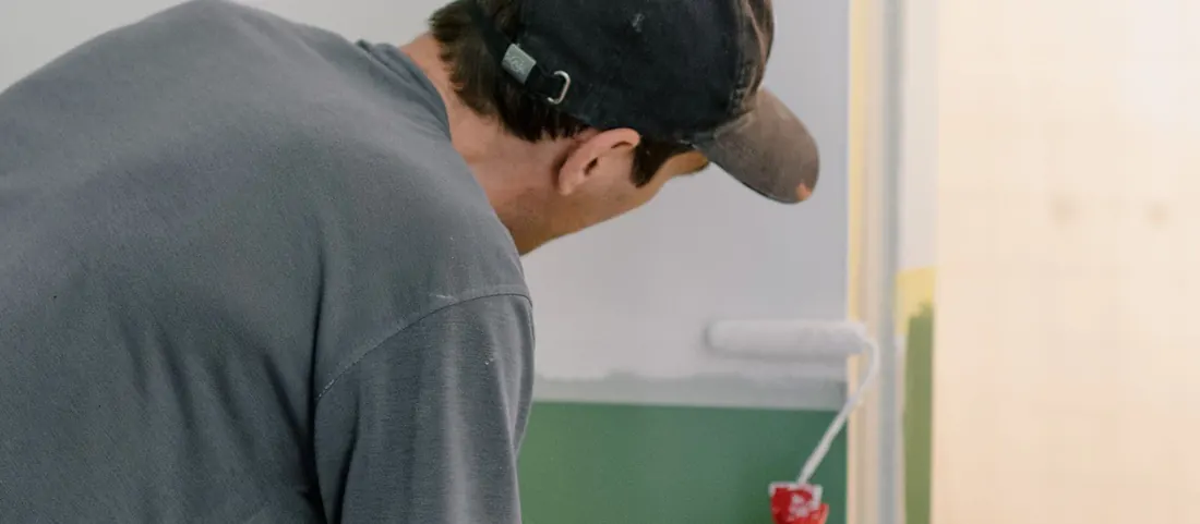 Painter cutting in a green wall with a small roller inside a room