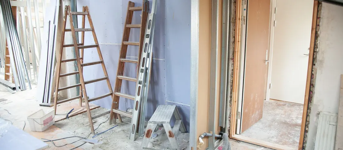 Room mid renovation with metal stud framing, drywall, ladders and a dusty floor