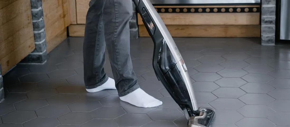 Cleaner running a vacuum head over grey hexagon floor tiles with dark grout lines