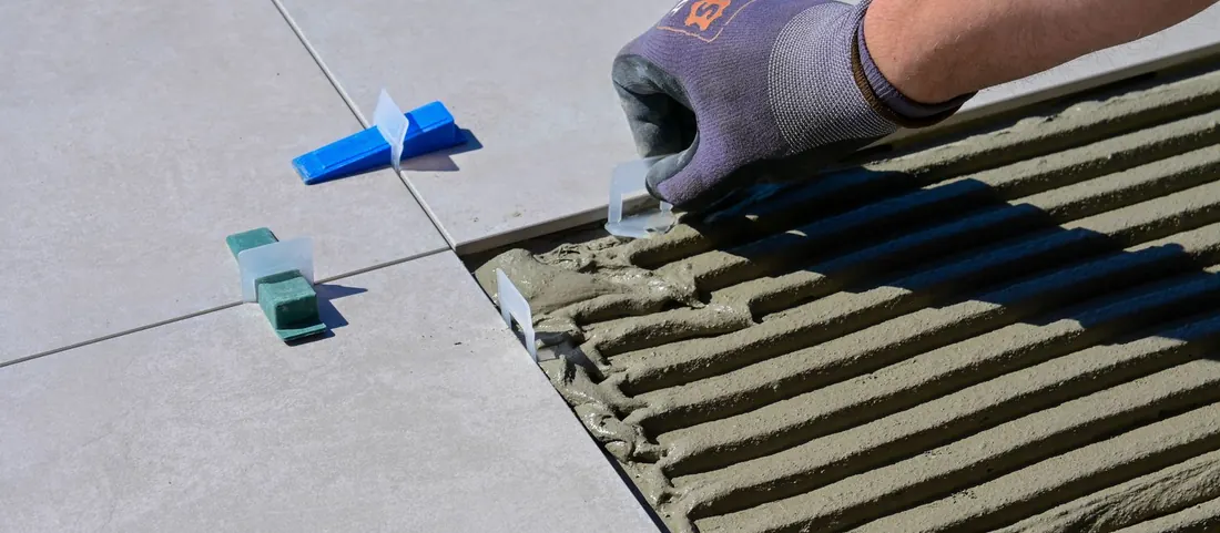 Gloved hand setting a floor tile into combed thinset beside levelling clips