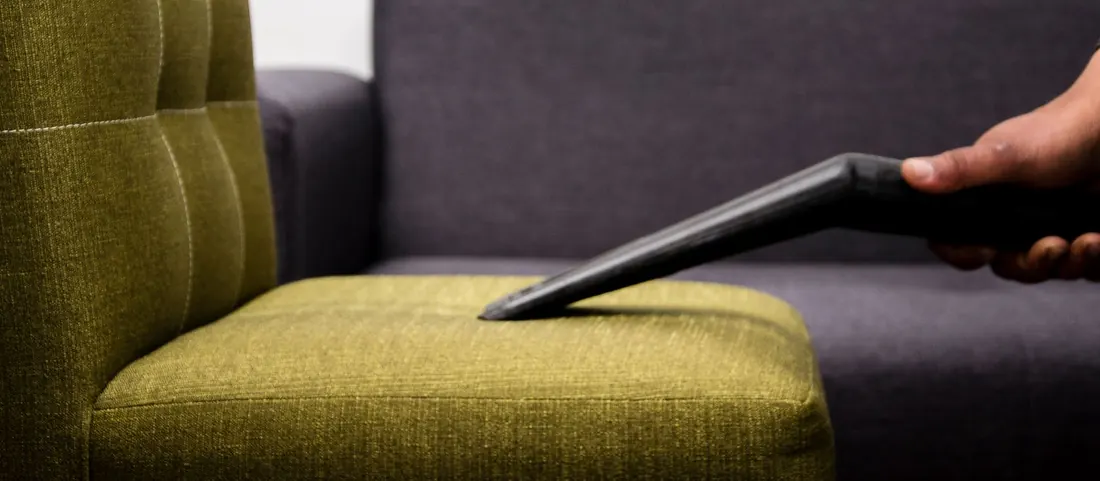 Upholstery nozzle cleaning the olive seat cushion of a chair beside a grey sofa