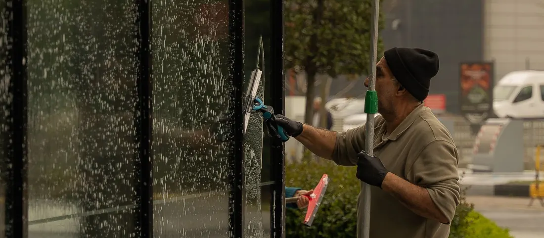 Window cleaner drawing a squeegee down the tall glass front of a building